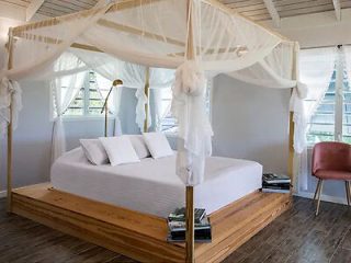 Elegant bedroom with a white four-poster bed, wooden floors, and sheer drapes